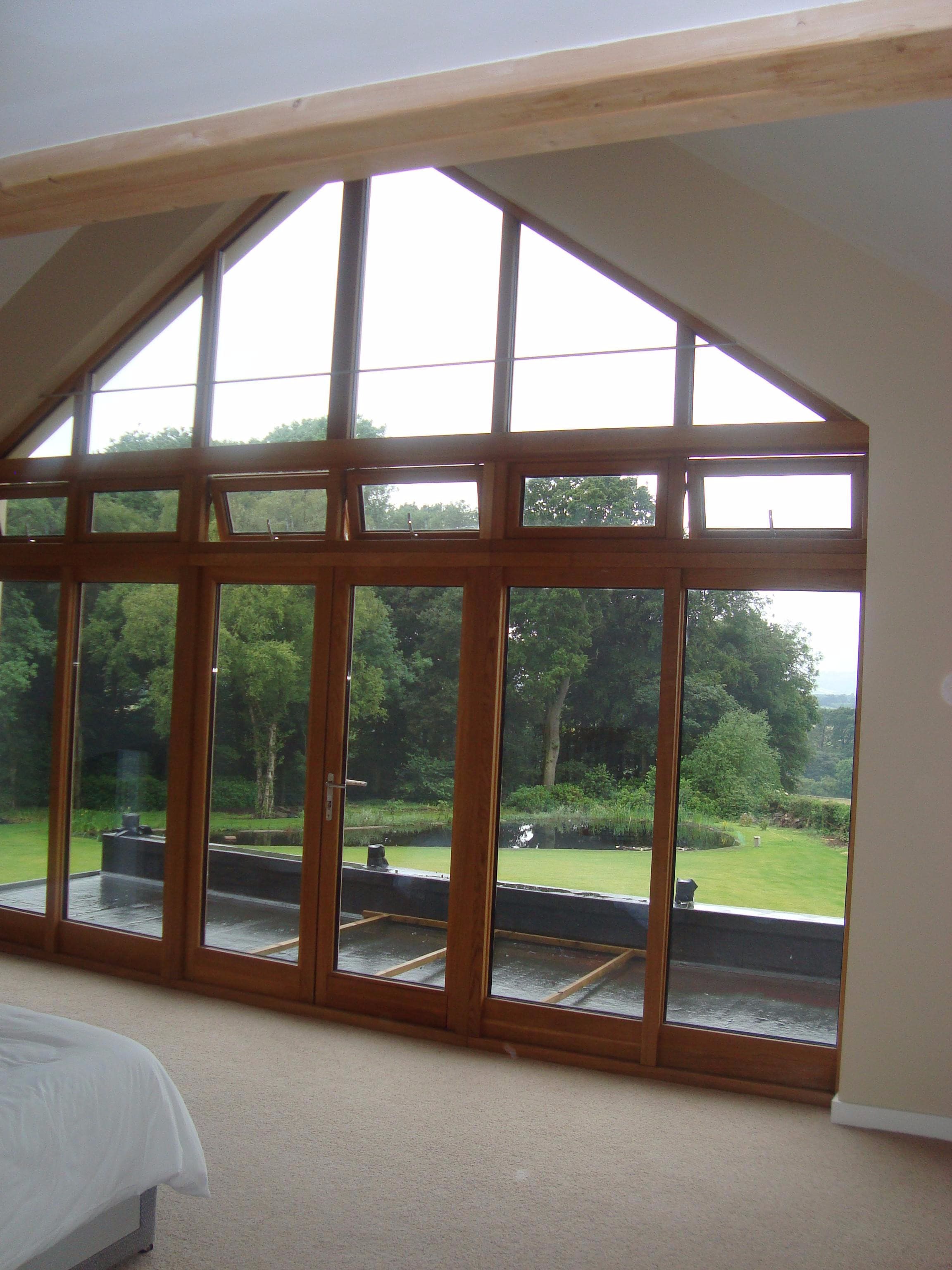 Bedroom with a full-height glazed gable overlooking a wooded garden